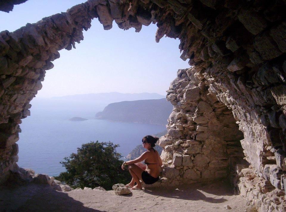 Luana sob um arco de pedra com o mar ao fundo